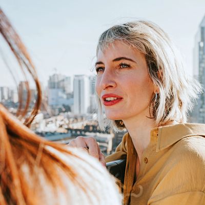 A woman leans up against a balcony and chats to another woman