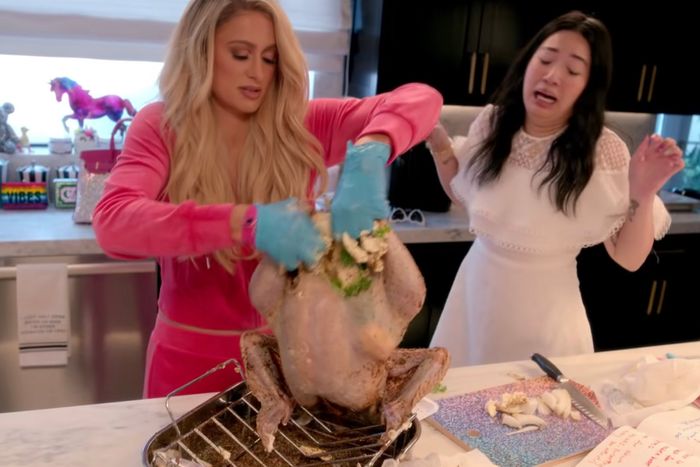A still from the Netflix show Cooking with Paris, featuring Paris Hilton stuffing a turkey as her assistant looks on, appalled. 