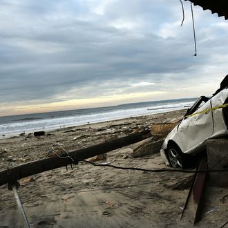 NEW YORK, NY - NOVEMBER 02: People walk on the beach near a damaged car and home in the Rockaway neighborhood, in Queens where a large section of the iconic boardwalk was washed away on November 2, 2012 in New York, United States. Limited public transit has returned to New York and most major bridges have reopened but will require three occupants in the vehicle to pass. With the death toll currently over 70 and millions of homes and businesses without power, the US east coast is attempting to recover from the effects of floods, fires and power outages brought on by superstorm Sandy. (Photo by Spencer Platt/Getty Images)