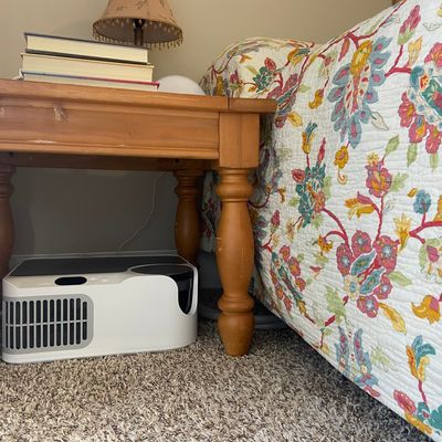 Bed with a floral quilt and a bedside table with a small control unit sitting underneath it. 