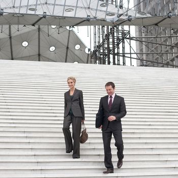 Two businesspeople outdoors coming down staircase
