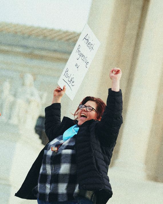 A woman with red hair and glasses holds a sign that reads 
