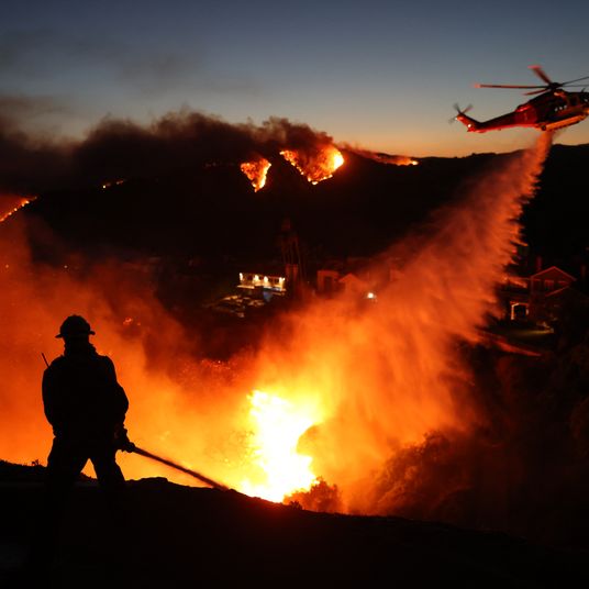 Fire personnel respond to homes destroyed while a helicopter drops water as the Palisades Fir