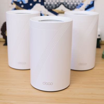 3 TP Link Deco router nodes sitting on a wooden desktop, arranged in a triangle.