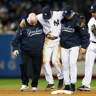 Derek Jeter #2 of the New York Yankees is carried off of the field by trainer Steve Donohue (L) and manager Joe Girardi after Jeter injured his leg in the top of the 12th inning against the Detroit Tigers during Game One of the American League Championship Series at Yankee Stadium on October 13, 2012 in the Bronx borough of New York City, New York.