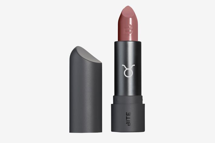 A subtle, muted rosy lipstick shade in a black lipstick tube that has the Taurus symbol on the front