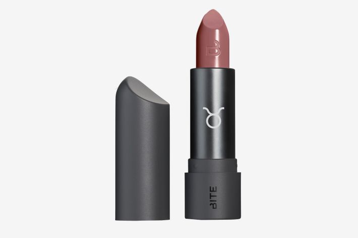 A subtle, muted rosy lipstick shade in a black lipstick tube that has the Taurus symbol on the front