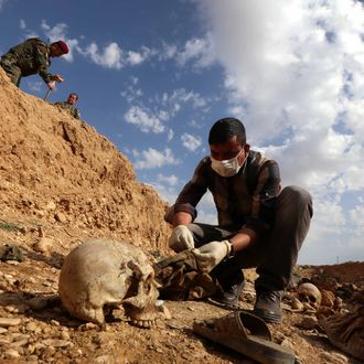 An Iraqi man inspects on February 3, 2015, the remains of members of the Yazidi minority killed by the Islamic State (IS) jihadist group after Kurdish forces discovered a mass grave near the village of Sinuni, in the northwestern Sinjar area. A peshmerga lieutenant colonel said the grave containing the remains of about 25 people was found during a search for explosives that IS often leaves behind, posing a threat to security forces and civilians even after they withdraw. AFP PHOTO / SAFIN HAMED (Photo credit should read SAFIN HAMED/AFP/Getty Images)
