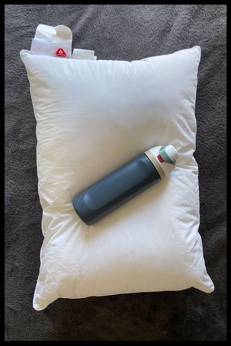A navy water bottle laying atop a while pillow.
