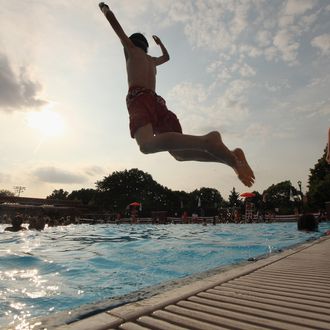 NEW YORK, NY - JUNE 28: A boy jumps as people bathe on opening day of the newly renovated McCarren Park Pool on June 28, 2012 in the Brooklyn borough of New York City. The historic 37,000 square-foot pool had been closed since 1983 but has been rejuvenated by a $50 million restoration. New York City public swimming pools opened today for the summer. (Photo by Mario Tama/Getty Images)