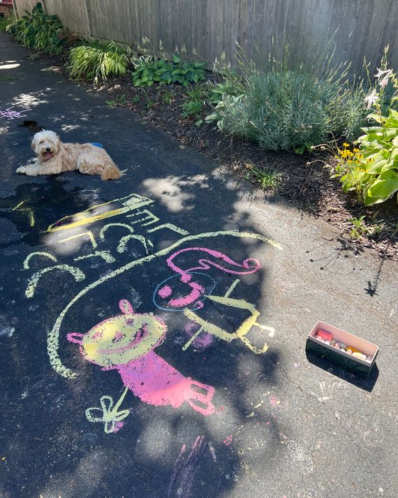 Yellow and pink chalk drawings and scribbles on a black driveway.