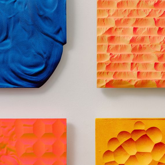 Blue, orange, and yellow rectangular-shaped sculptures that are hung on a wall like canvases