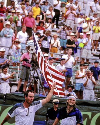 John McEnroe and Andre Agassi race around the stadium with the american flag after winning the 1992 Davis Cup. (Photo by Al Messerschmidt/Getty Images)