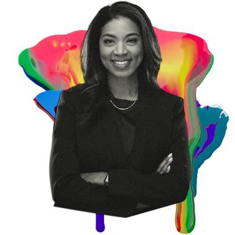 A black woman wearing a black blazer smiles for a portrait. She's wearing her long hair in a loose wave over her shoulder and crosses her arms over her chest.