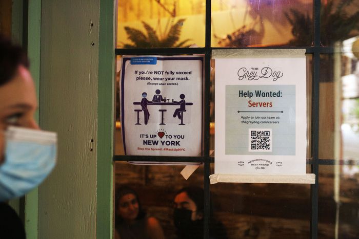 A Manhattan restaurant window with two paper signs: one explaining masks are required for unvaccinated patrons, and the other advertising 'help wanted.'