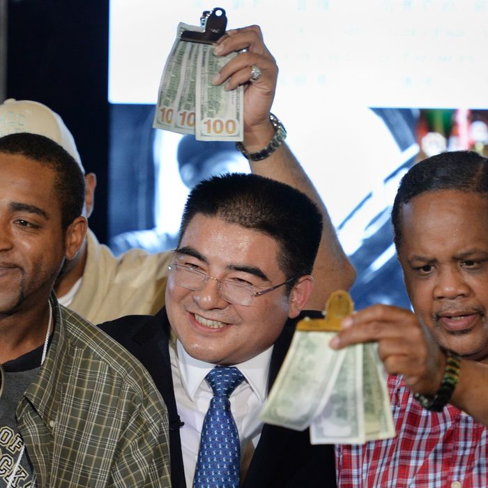 Chinese philanthropist Chen Guangbiao (C) poses with men holding gifts of money as he hosts a lunch for several hundred homeless people from the New York City Rescue Mission June 25, 2014 at The Boathouse restaurant in New York's Central Park. Chen also was to give USD $300 to each participant in the lunch. AFP PHOTO/Stan HONDA (Photo credit should read STAN HONDA/AFP/Getty Images)