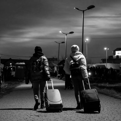 Two women wearing hats and puffer jackets pull backpacks behind them as they arrive at Poland's border with Ukraine. 