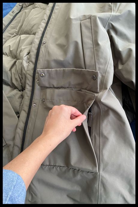 Close up photo of a hand revealing the secret zipper pocket behind the patch pockets on Quince's Women's Responsible Down Hooded Long Parka. 