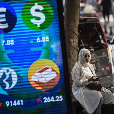 A woman sits beside a digital billboard giving updates on various currencies and the Turkish stock exchange in Istanbul.