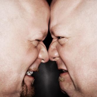 Close up of Caucasian bald mid adult identical twin men standing face to face with angry expression.