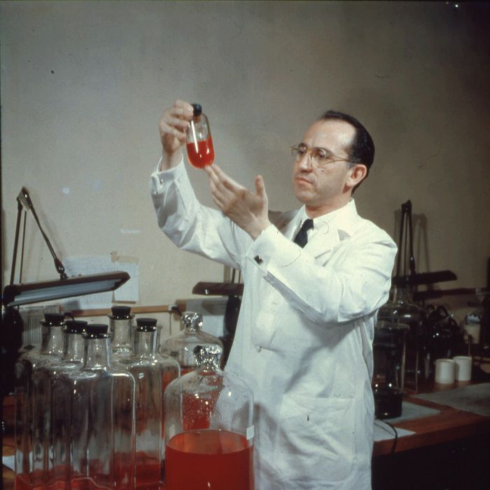 View of American scientist and physician Jonas Salk (1914 - 1995), developer of the polio vaccine, wearing a white lab coat, and smiling while holding up a bottle in the laboratory, mid twentieth century. (Photo by Archive Photos/Getty Images)