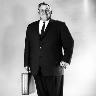 A portly gentleman in a business suit, carrying an attache case and smiling broadly.