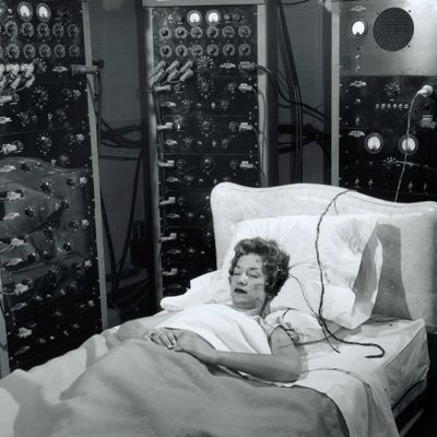 A woman sleeps in a bed surrounded by electronic monitoring equipment.
