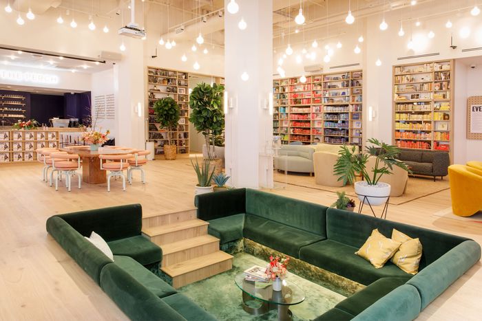 A view of a coworking office with a green velvet conversation pit and color-coded bookshelves in background