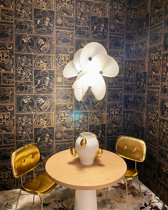 room with black wallpaper with intricate gold drawings and gold chairs