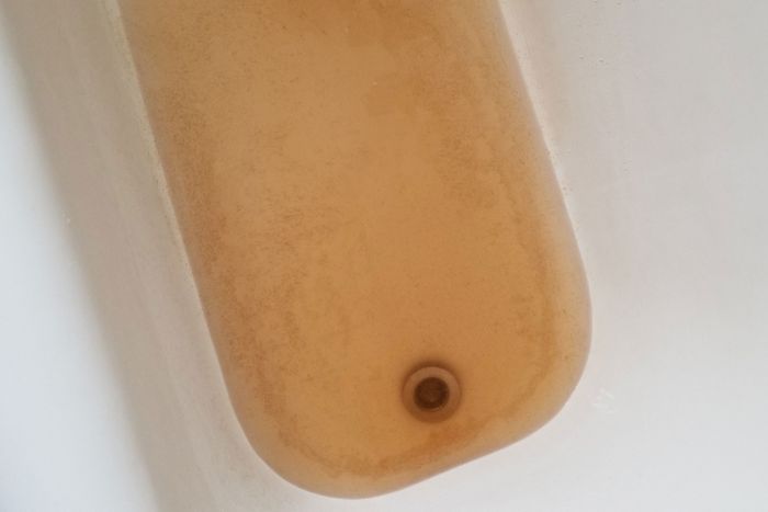Brown water filling a bathtub, seen from above.
