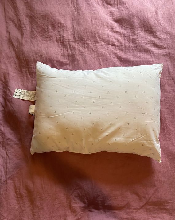 A white pillow on a pink duvet.
