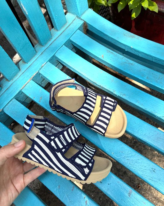 Photo of an adult hand holding Rothy's The Double Strap Sandal in size little kid 8.