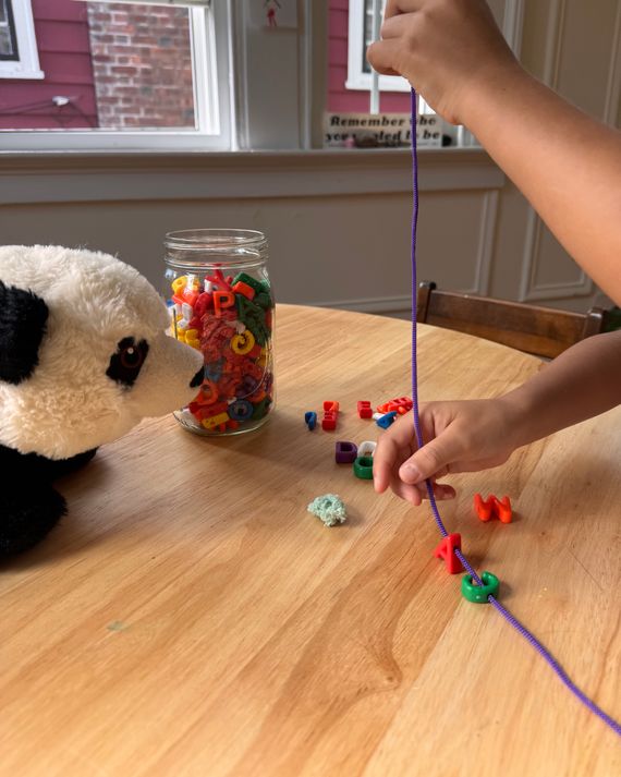 A child stringing alphabet letter beads on a purple lacing string.