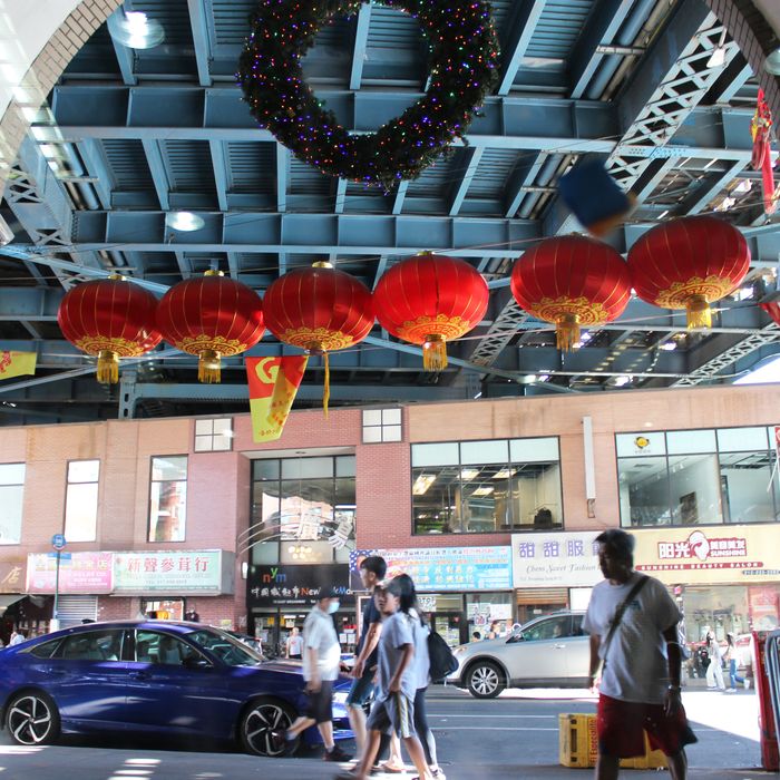 A row of red lanterns hangs in a doorway, to a view of a brick shopping center with Chinese-language signs.