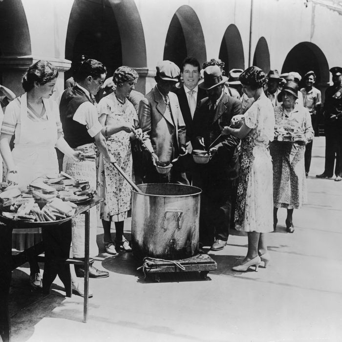 1930: Unemployed men receiving soup and slices of bread in an outdoor breadline during the Great Depression, Los Angeles, California. Some women serve the soup with large ladles while others hand out slices of bread from trays. (Photo by American Stock/Getty Images)