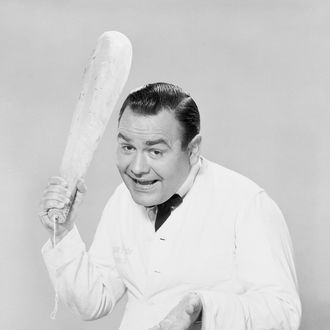 Jonathan Winters brandishes a loaf of bread, acting the part of a waiter at a large restaurant asking for a tip.