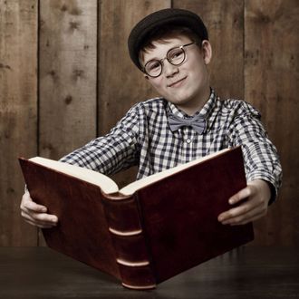 Young boy in retro clothing wearing spectacles holding a massive book --- Image by ? 13/PeopleImages.com/Ocean/Corbis