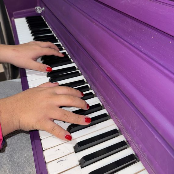 A girl&rsquo;s hands, nails painted red, play the keys of a purple piano.