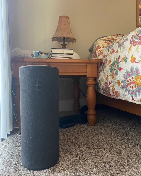 A large, black computer-like object next to a nightstand and bed.