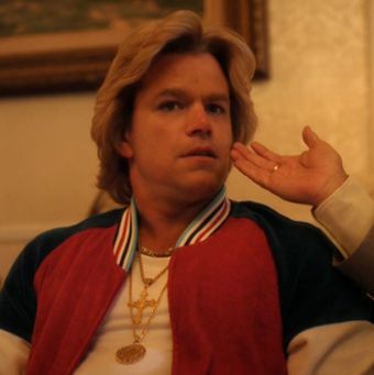 Multiple necklaces are wrapped around a prosthetically enhanced flabby neck. The facial features are still Damon's, and it's the last time you'll see them in their natural state.