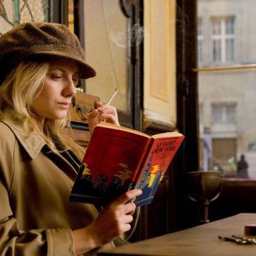 Melanie Laurent, reading a book and smoking a cigarette in a Parisian cafe