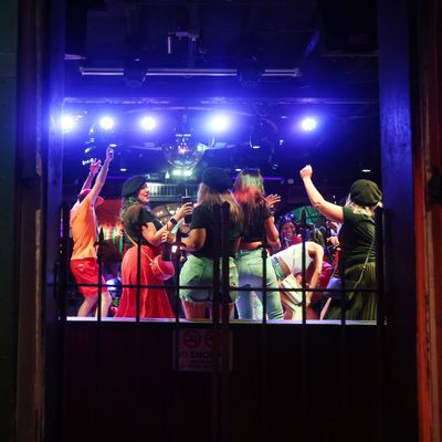 People dancing maskless in a bar next to a sign that says wear a mask.