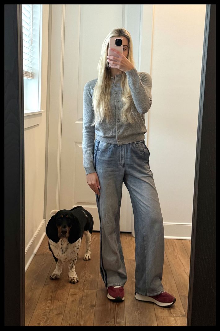 A woman taking a mirror selfie while wearing a gray sweater, sneakers, and the Rag & Bone Miramar Wide-Leg Track Pants, with a dog in the background.