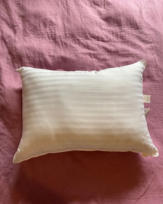 A white pillow on a pink duvet.