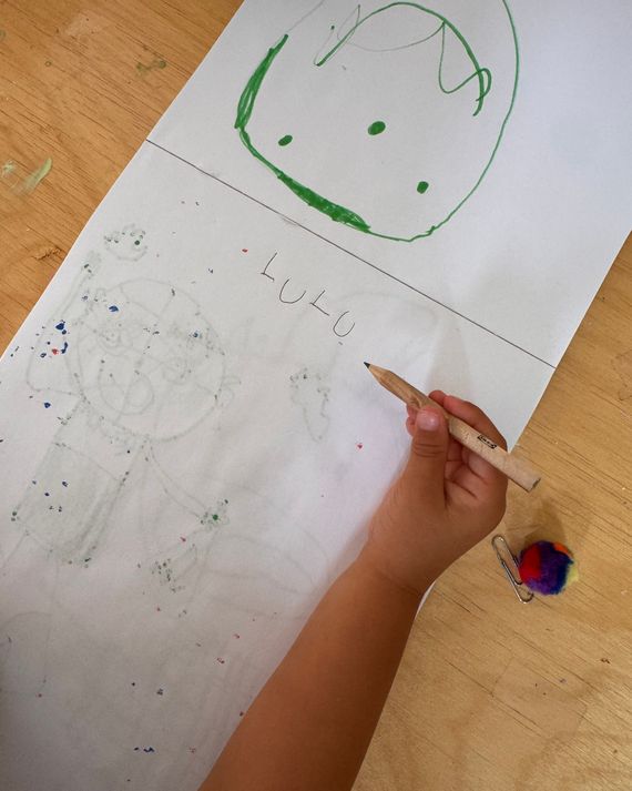 A child's hand holding an Ikea pencil to write on a piece of paper.