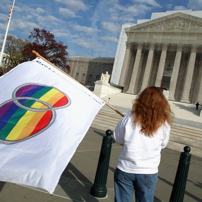 WASHINGTON, DC - NOVEMBER 30: Same-sex marriage proponent Kat McGuckin of Oaklyn, New Jersey, holds a gay marriage pride flag while standing in front of the Supreme Court November 30, 2012 in Washington, DC. With the Supreme Court building draped in a photo-realistic sheet during a repair and preservation project, the justices met today to consider hearing several cases dealing with the rights of gay couples who are married, want to get married or are in domestic partnerships. (Photo by Chip Somodevilla/Getty Images)