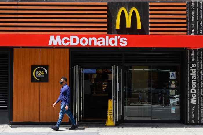 A person in a mask walking past a McDonald's on a sunny day