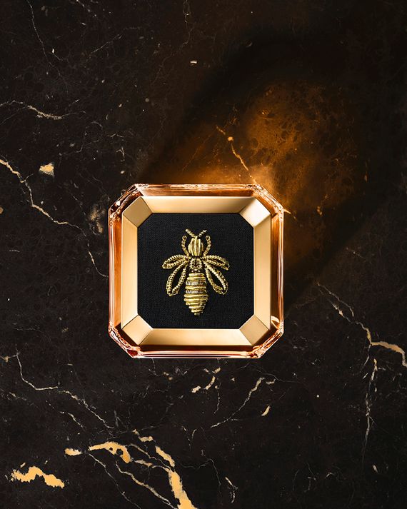 An overhead view of a limited-edition plate on a Guerlain perfume bottle. The plate is black and embossed with a gold bee.