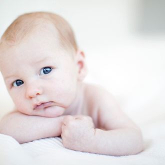 Portrait of baby boy resting chin on hands while lying in bed.