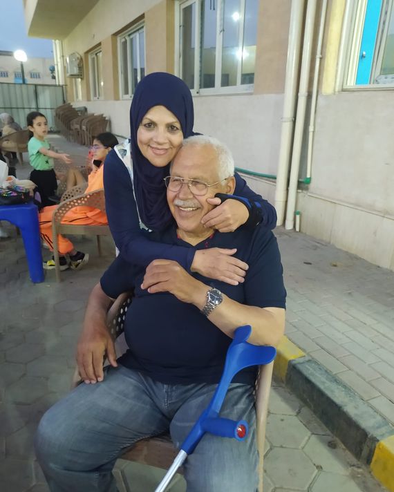 Una mujer que lleva hijab abraza a un hombre con gafas, que está sentado en una silla con un bastón a su lado.